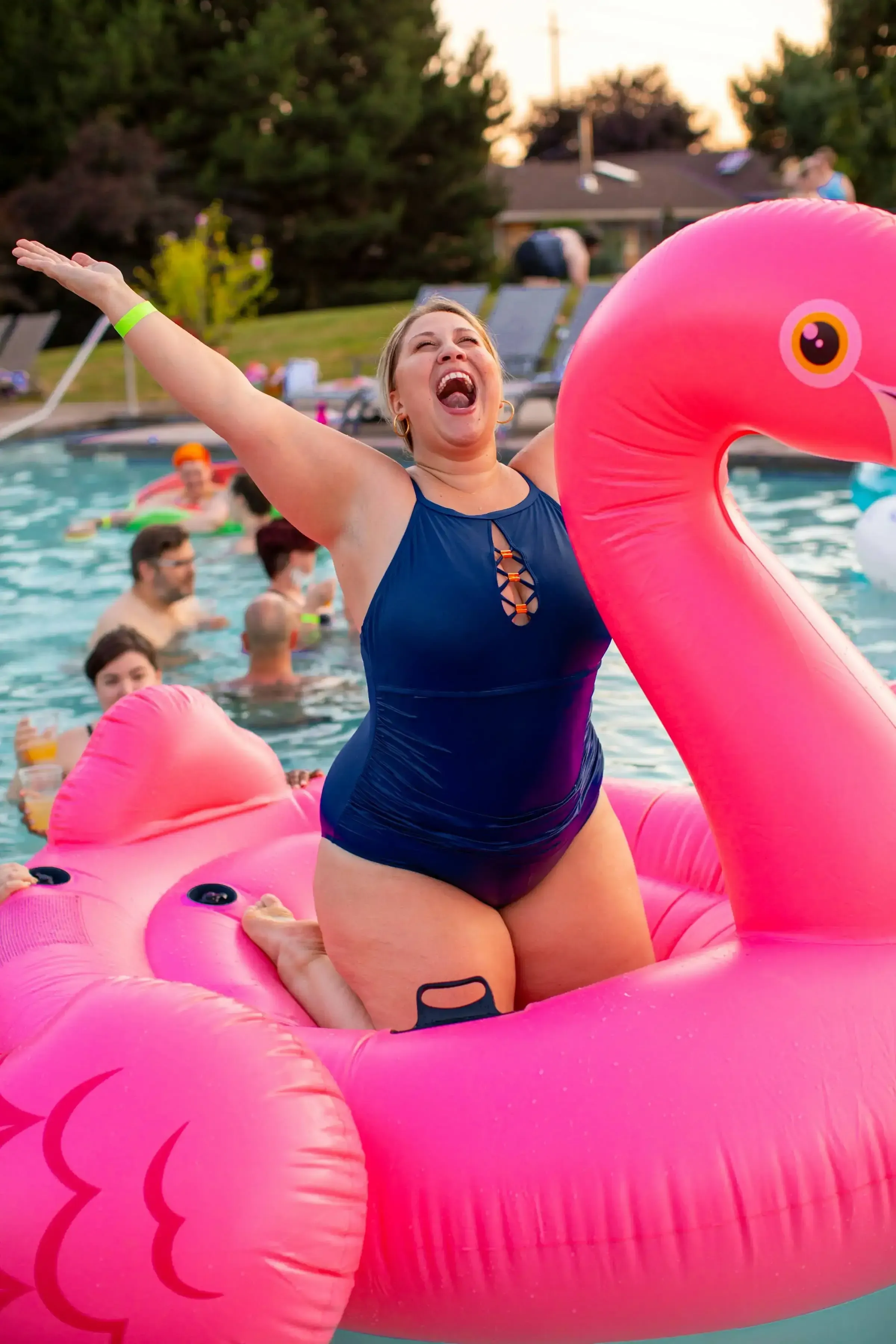 a woman laughing with her arms in the air on a flamingo water float