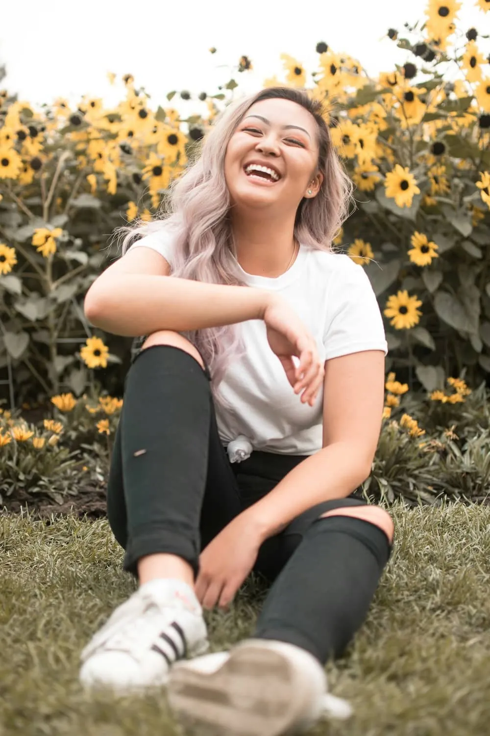 a woman smiling joyfully while comfortably sitting in front of a bed of yellow flowers