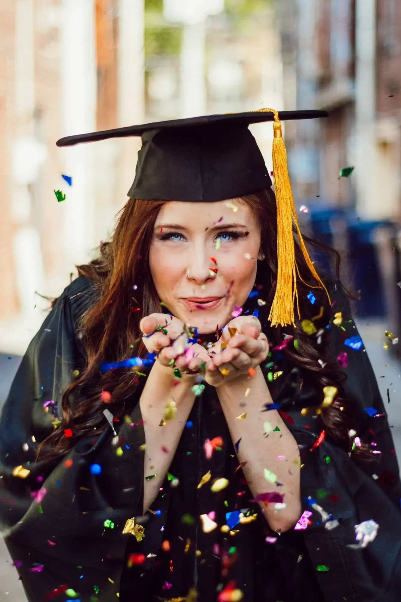 a woman blowing assorted color confettis in a graduation outfit