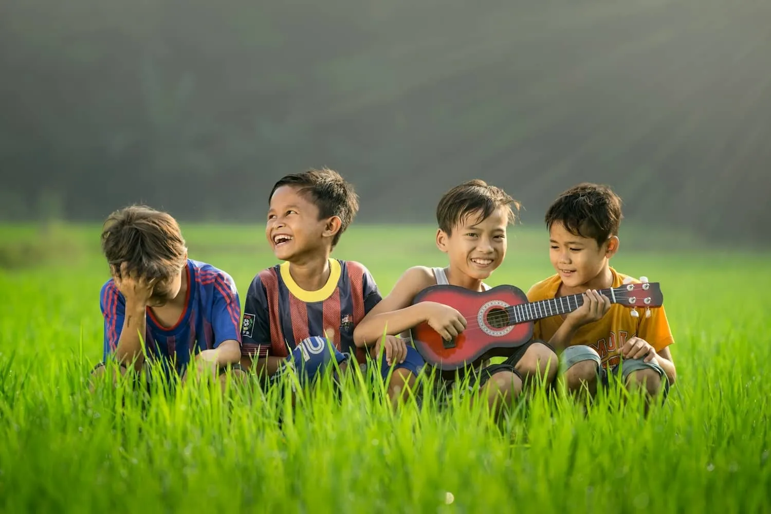 Four children sitting together laughing and playing in the grass